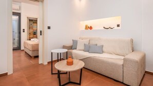 A modern living room with a beige sofa, two side tables, and a small orange vase. - Emma's Central Suite (Kos)