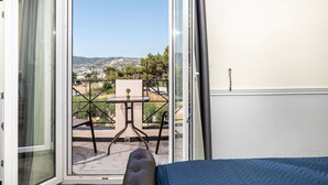 Un balcón con mesa y sillas, vista a un paisaje lejano y una cama con cubrecama azul.