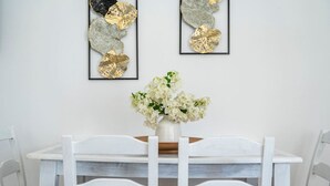 Spisebord med hvide stole, en vase med hvide blomster og to indrammede abstrakte kunstværker på væggen.