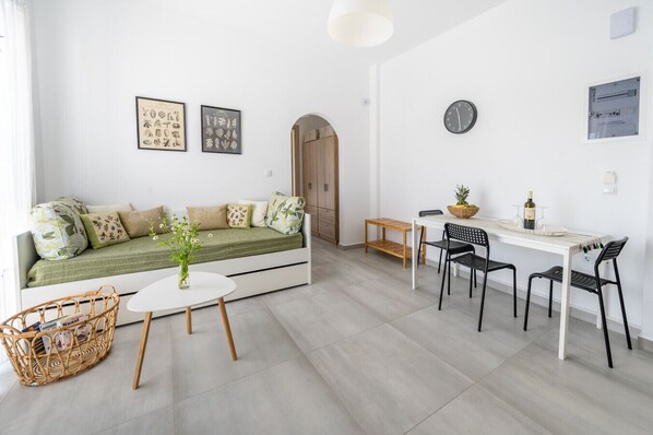 A modern living room with a sofa, a dining table with chairs, a small side table, and a wicker basket.