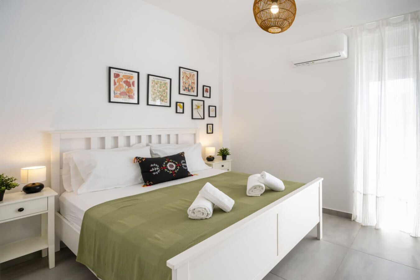 Un dormitorio ordenado con cama, mesita de noche, lámpara, aire acondicionado instalado en la pared y cuadros enmarcados.
