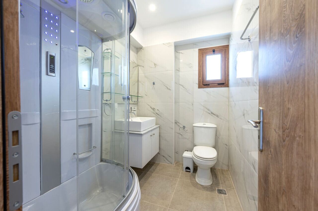 A modern bathroom with a glass-enclosed shower, a toilet, and a sink.