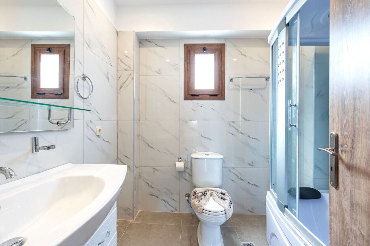 Une salle de bain avec un mur en marbre, une douche en verre, des toilettes blanches et une grande baignoire.