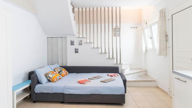 A modern bedroom with a grey sofa bed, a small desk, and a staircase leading to an upper level. - Sunrise Beachfront Getaway (Kardamaina)