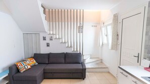 A modern living room with a grey sofa, a colorful pillow, a staircase, and a white door. - Sunrise Beachfront Getaway (Kardamaina)