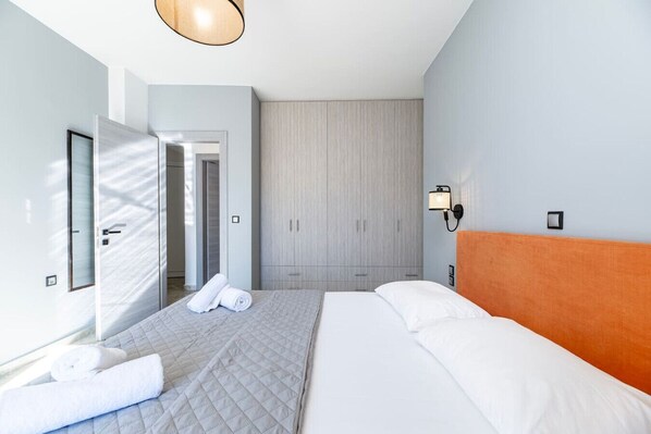 A modern hotel room with a bed, a wardrobe, a mirror, and a wall-mounted light fixture.