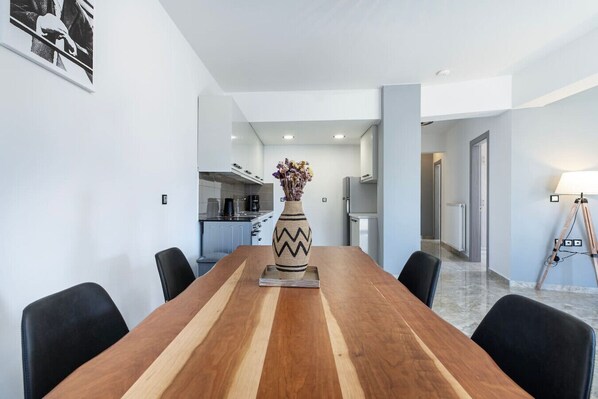 A modern dining area with a wooden table, chairs, a decorative vase, and a kitchen in the background.