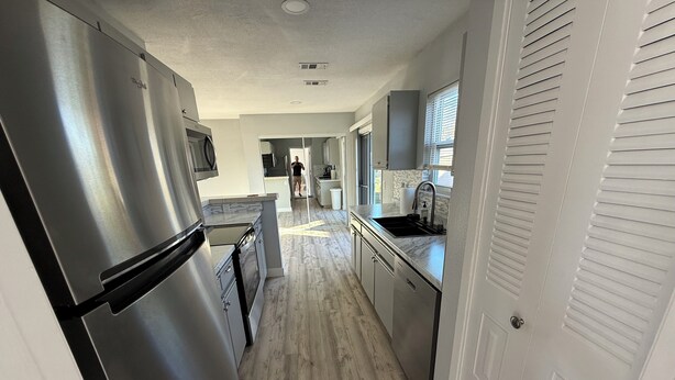 A modern kitchen with stainless steel appliances, a wooden floor, and a view into the living area.