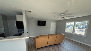 A spacious living area with a large window, a ceiling fan, and a kitchen area with a countertop.