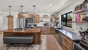 Une cuisine moderne avec des meubles en bois, un îlot central, des luminaires suspendus et une grande fenêtre qui laisse entrer la lumière naturelle.