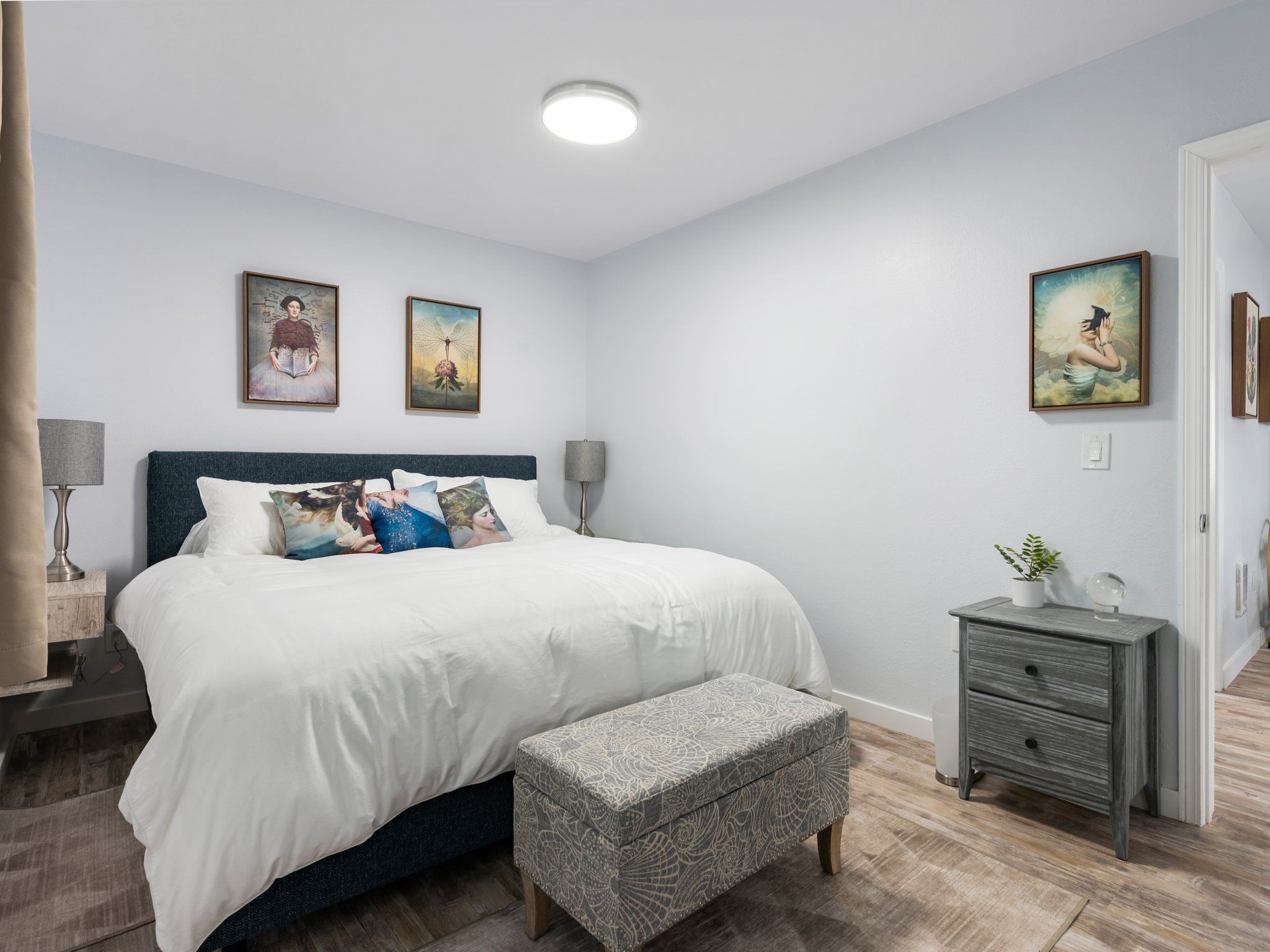 A neatly arranged bedroom with a large bed, bedside tables, a bench, and artwork on the walls.