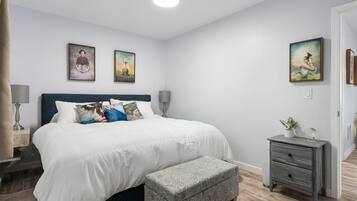 A neatly arranged bedroom with a large bed, bedside tables, a bench, and artwork on the walls.