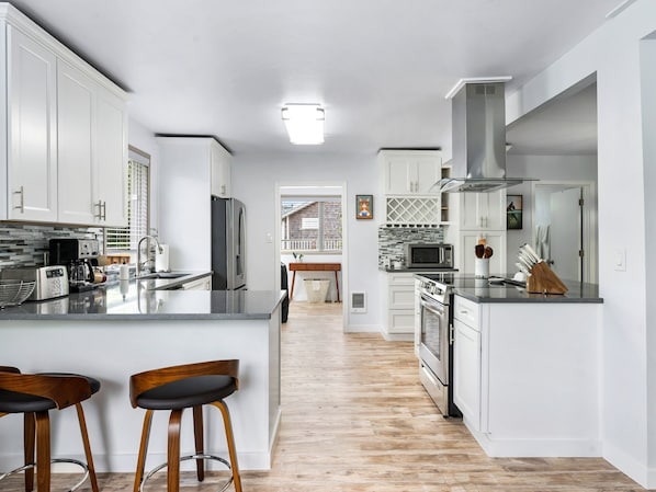Una cocina moderna con armarios blancos, una isla grande con taburetes de bar, un microondas y una campana extractora de acero inoxidable.
