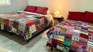 Une chambre avec deux lits, chacun recouvert d’une couverture aux couleurs vives. Une lampe se trouve sur une table de chevet entre les deux lits.