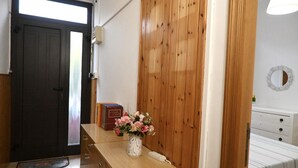 Een kamer met een houten deur, een houten wand, een witte ladekast, een vaas met bloemen en een spiegel aan de muur.