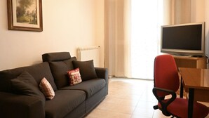 Een woonkamer met een bank, een rode fauteuil, een televisie en een schilderij aan de muur.