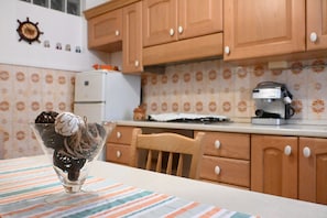 Una cocina con armarios de madera, un refrigerador, una cafetera y un cuenco decorativo sobre la mesa.