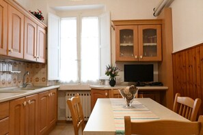 Una cocina con armarios de madera, un ventanal, una mesa de comedor con sillas y un televisor.