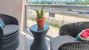 A balcony with wicker furniture, a potted plant, and a view of a road and greenery. - Cozy 2 bethoom apartament (Andrés)