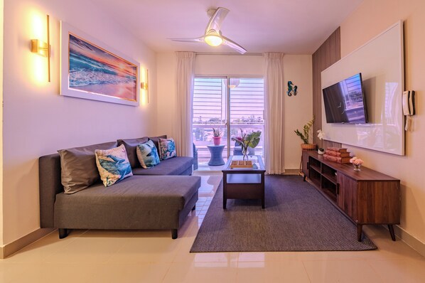 A modern living room with a sofa, coffee table, TV, and a balcony with plants.