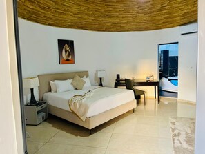 A hotel room with a bed, bedside tables, a desk, and a view of a cityscape. - SEN HOTEL (Mbour)