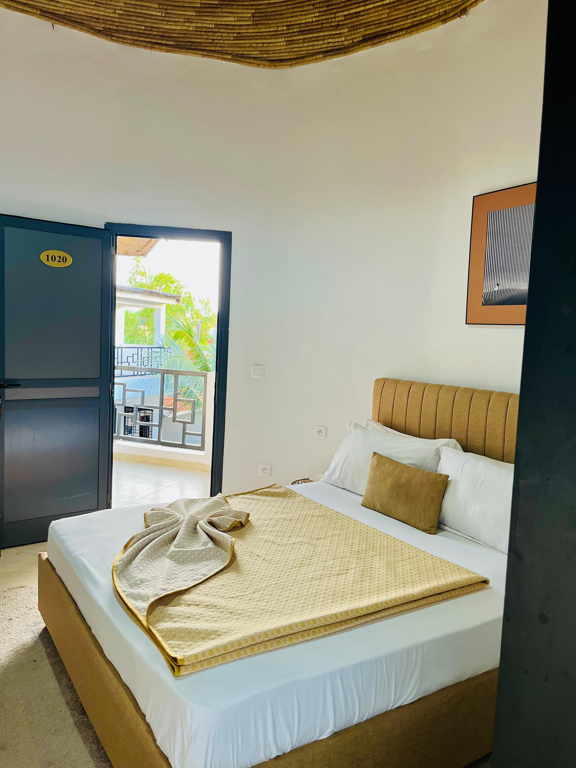 A hotel room with a bed, a door, a window, and a view of the outside.