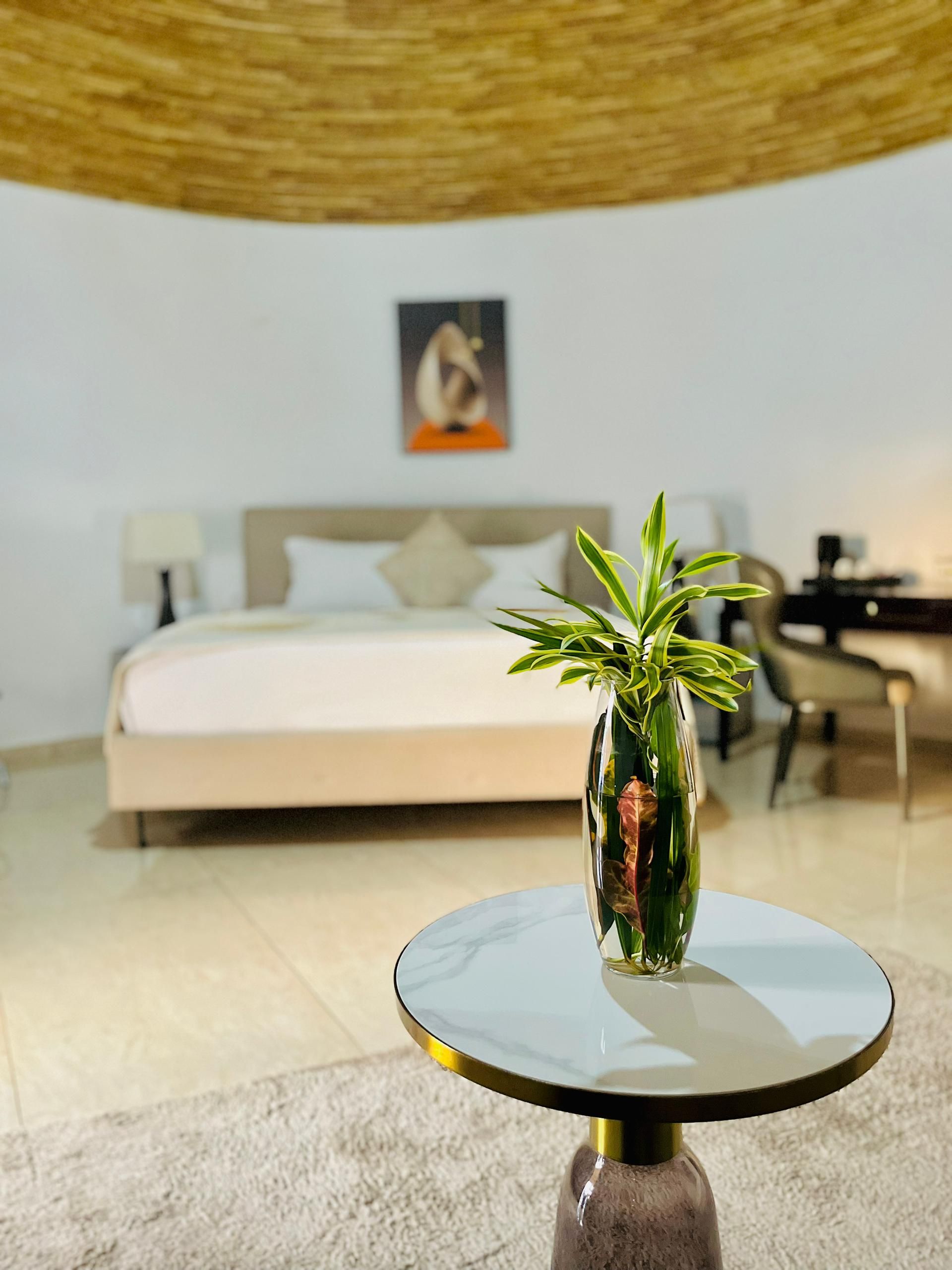 Ein modernes Schlafzimmer mit einem Bett, einem Schreibtisch und einem runden Tisch mit einer Vase grüner Pflanzen.