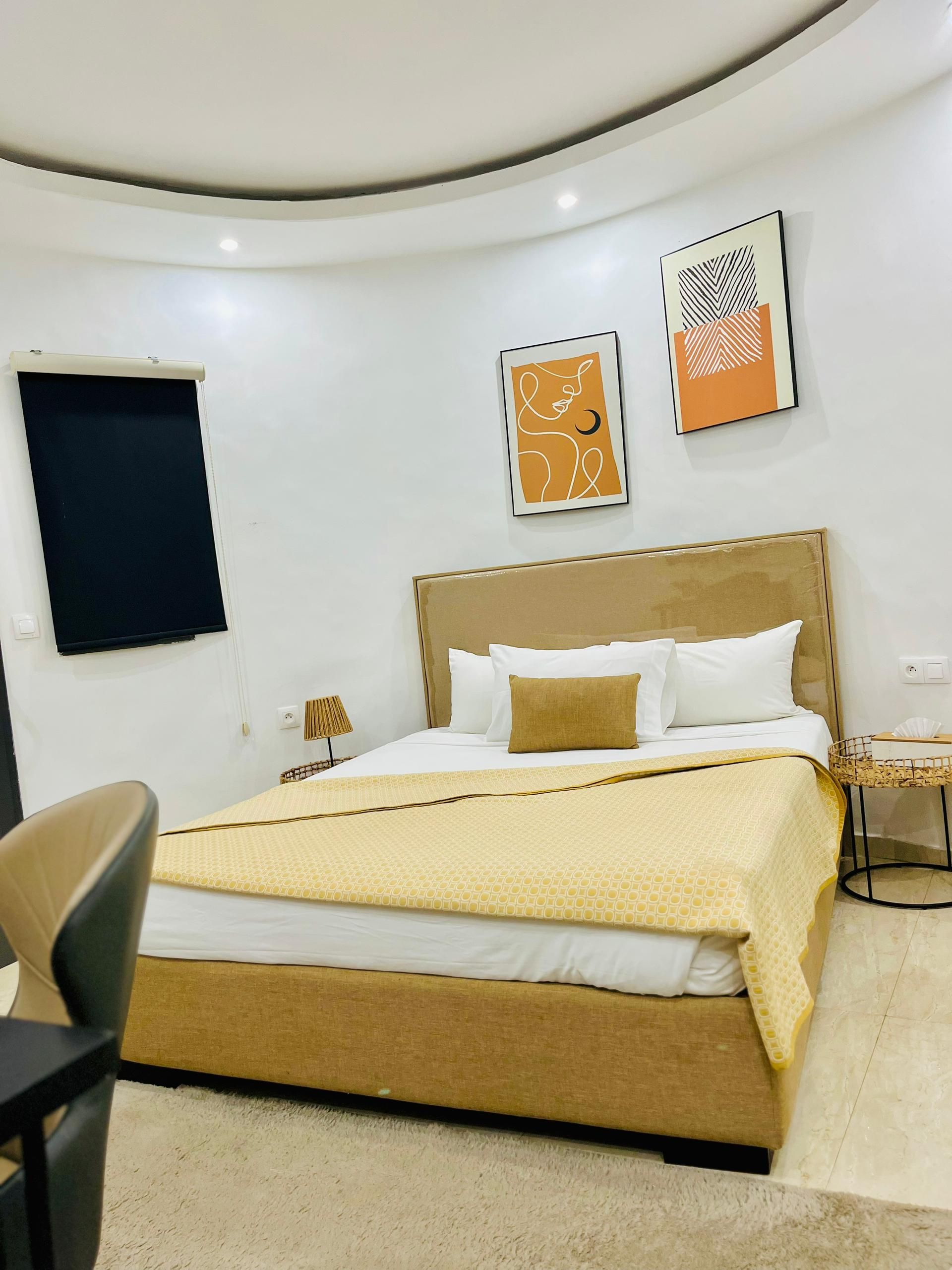 A modern hotel room with a large bed, a desk, and two framed artworks on the wall.