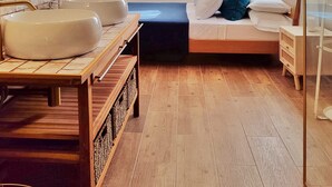 A modern bathroom with a large mirror, two sinks, a wooden vanity, and a bed with a blue mattress and teal pillows. - Casa Rosetta Boutique (Xàtiva)