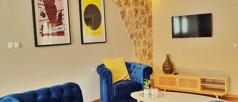 A living room with a blue sofa, a small coffee table, a TV mounted on the wall, and two framed pictures on the wall.