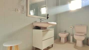 A bathroom with a white vanity, a mirror, a sink, a bidet, and a toilet.