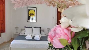 A bedroom with a bed, pillows, a framed picture on the wall, and a vase with flowers.