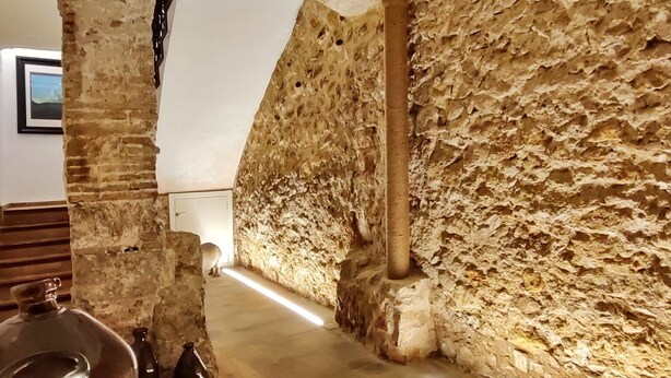 A stone-walled room with a sloped ceiling, a large window, and a long, narrow table with chairs. - Casa Rosetta Boutique (Xàtiva)