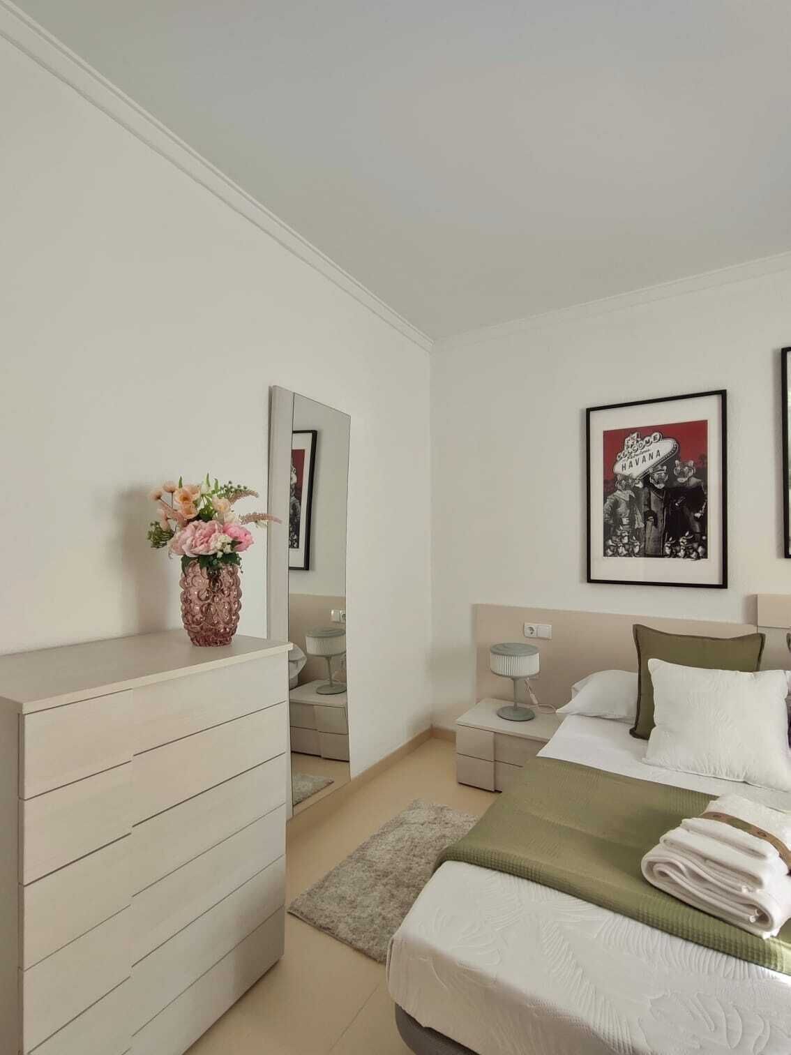 A modern bedroom with a bed, bedside tables, a dresser, and a mirror.
