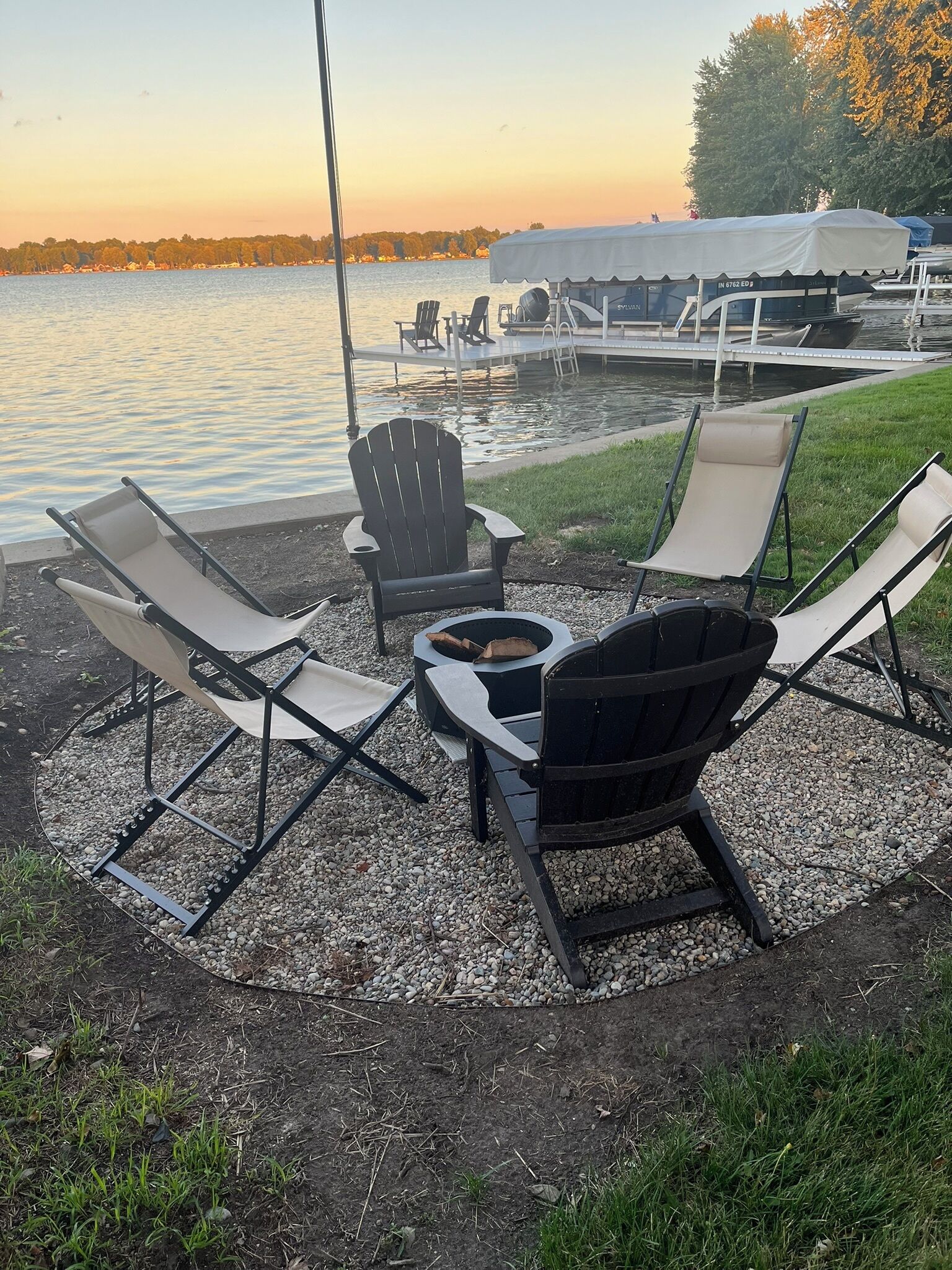 Un espace de détente aménagé au bord du lac, avec des fauteuils Adirondack, un foyer et une table couverte.