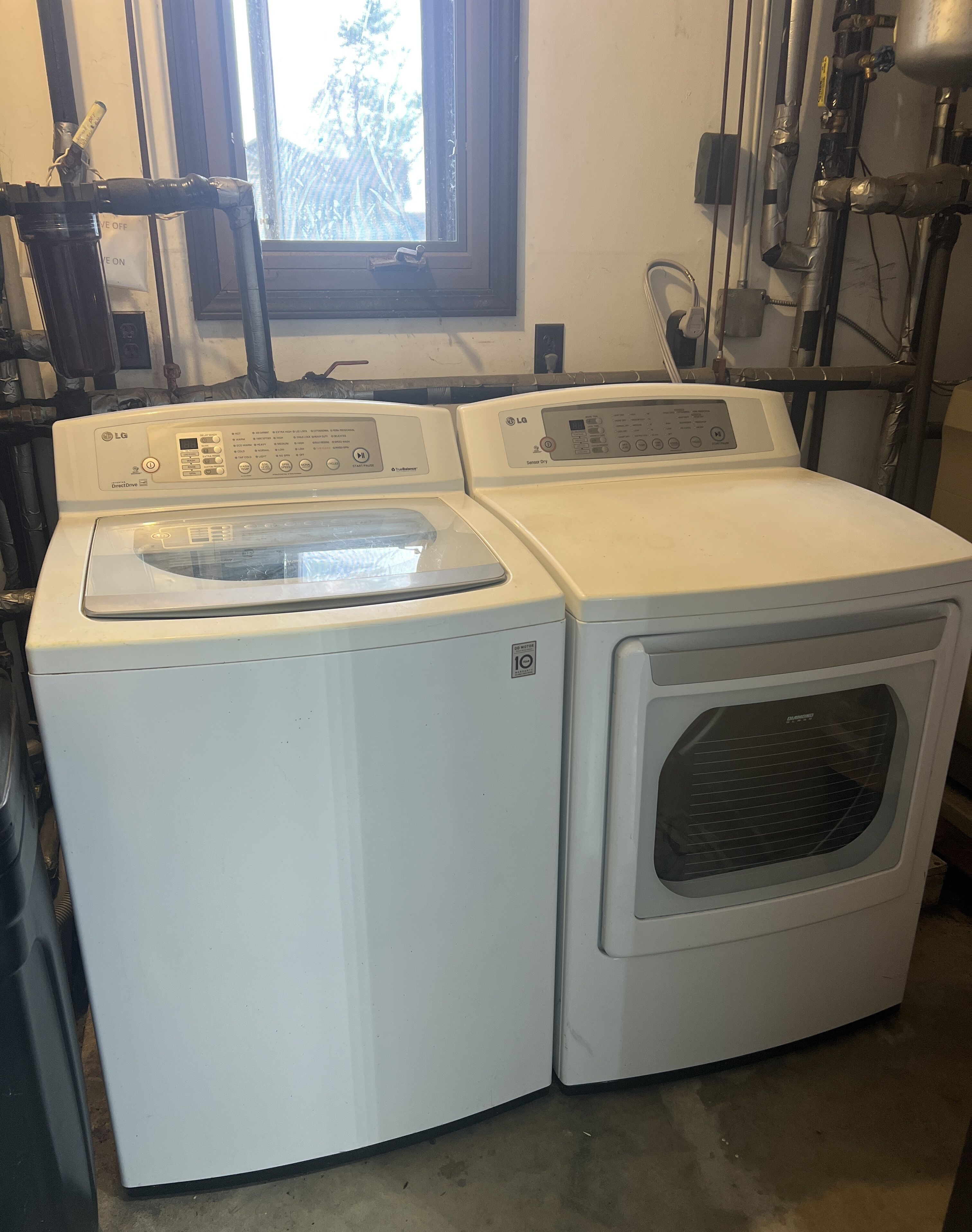 A laundry room with two stacked washing machines, a window, and visible plumbing.