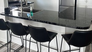 A modern kitchen with a black marble countertop, stainless steel appliances, and black bar stools.