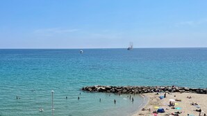 A beach with clear turquoise waters, a rocky breakwater, and a sailboat in the distance. - Tre Ponti Beach Apartment - sea view (Sanremo)