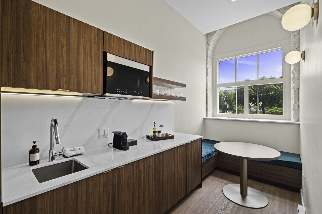 A modern kitchen with a built-in stove, a sink, and a window with a view of greenery.