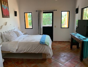 Ein Schlafzimmer mit einem Bett, einem Schreibtisch, einem Fernseher und zwei Fenstern mit Vorhängen.