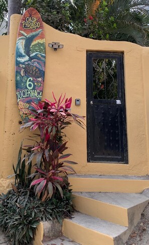 A building with a yellow exterior, a black door, and a colorful sign with a tree and the number 6. - Casa Paraiso with AC, Wi-Fi, Pool, water filtration, full concierge service. (Sayulita)