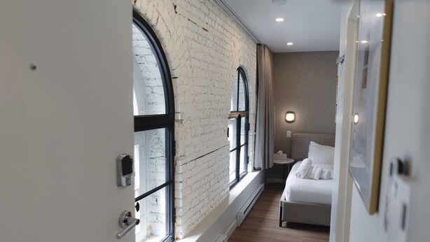 A room with a brick wall, large arched windows, a bed, and a bedside table.