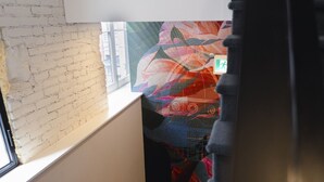 Ein Zimmer mit Backsteinwand, Fenster und einem farbenfrohen, abstrakten Wandbehang.