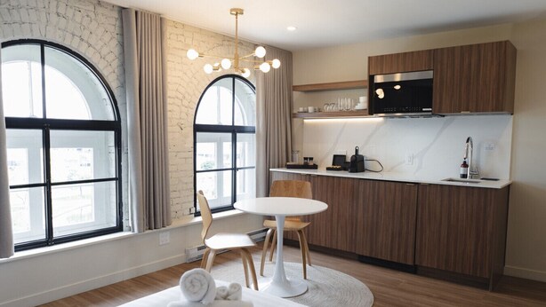 Une cuisine moderne équipée d’un four à micro-ondes, d’une cuisinière et d’un évier, une table de salle à manger ronde avec des chaises, et de grandes fenêtres avec des rideaux.