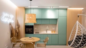 Una cucina moderna con armadietti color petrolio, una lampada a sospensione e un tavolo da pranzo rotondo con sedie in vimini.