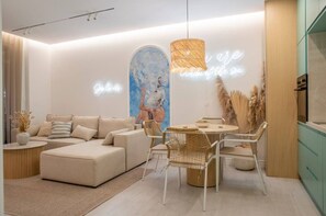 Una sala moderna con sofá, mesa de comedor y sillas, un cuadro abstracto grande y un letrero de neón en la pared.