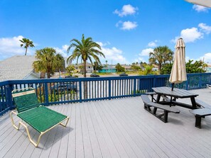 A wooden deck with a blue railing, a green lounge chair, and picnic tables.
