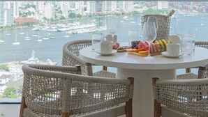 A round table with wicker chairs, a breakfast setting, and a view of a marina and cityscape. - Premium suite 25th floor (Cartagena de Indias)