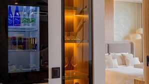 A modern hotel room with a built-in LG refrigerator, a glass-fronted shelving unit, and a neatly made bed. - Premium suite 25th floor (Cartagena de Indias)