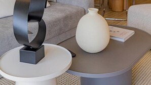 A modern living room with a grey sofa, a round coffee table with a vase, and a minimalist sculpture. - Premium suite 25th floor (Cartagena de Indias)